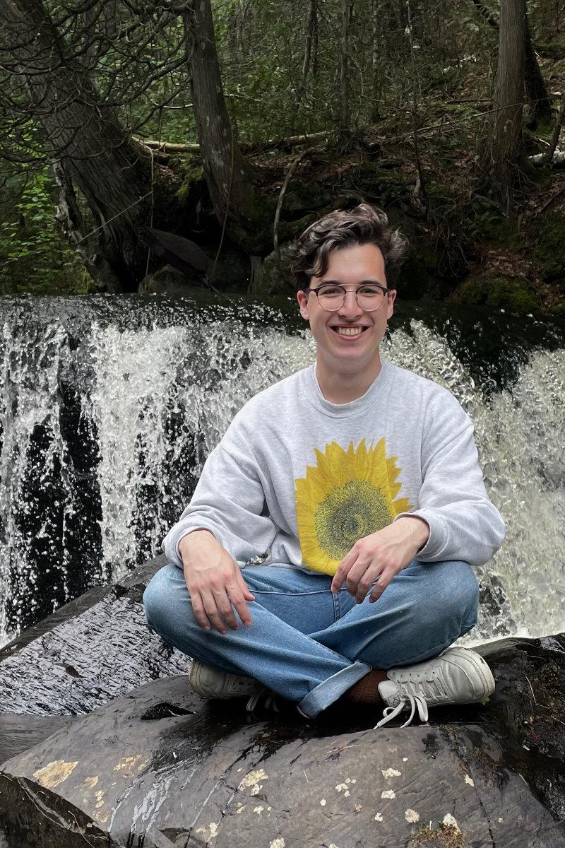 Paul Kawabe sitting on a rock in front of a waterfall